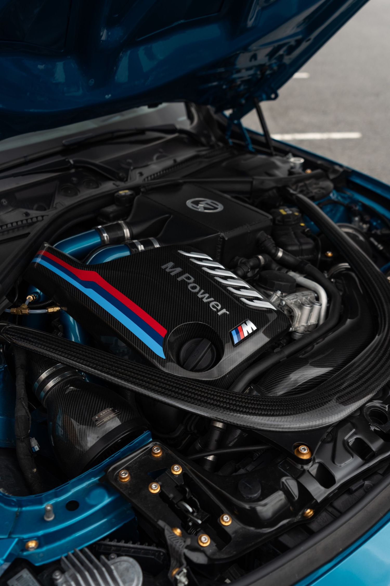 Close-up view of a BMW M-series engine bay featuring iconic M-Power badging and BMW's signature blue and red stripes.