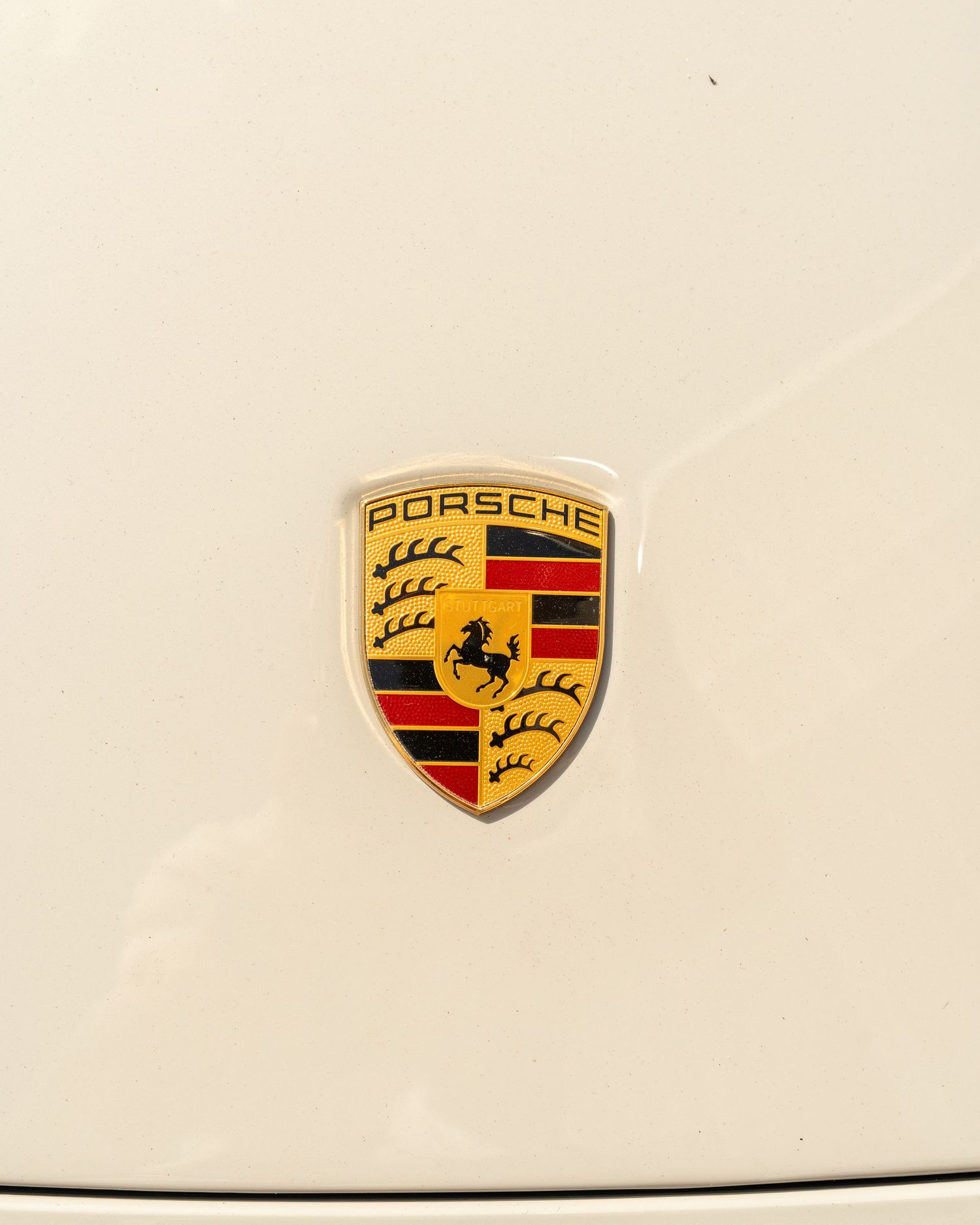 Close-up shot of classic Porsche emblem badge on white paint.