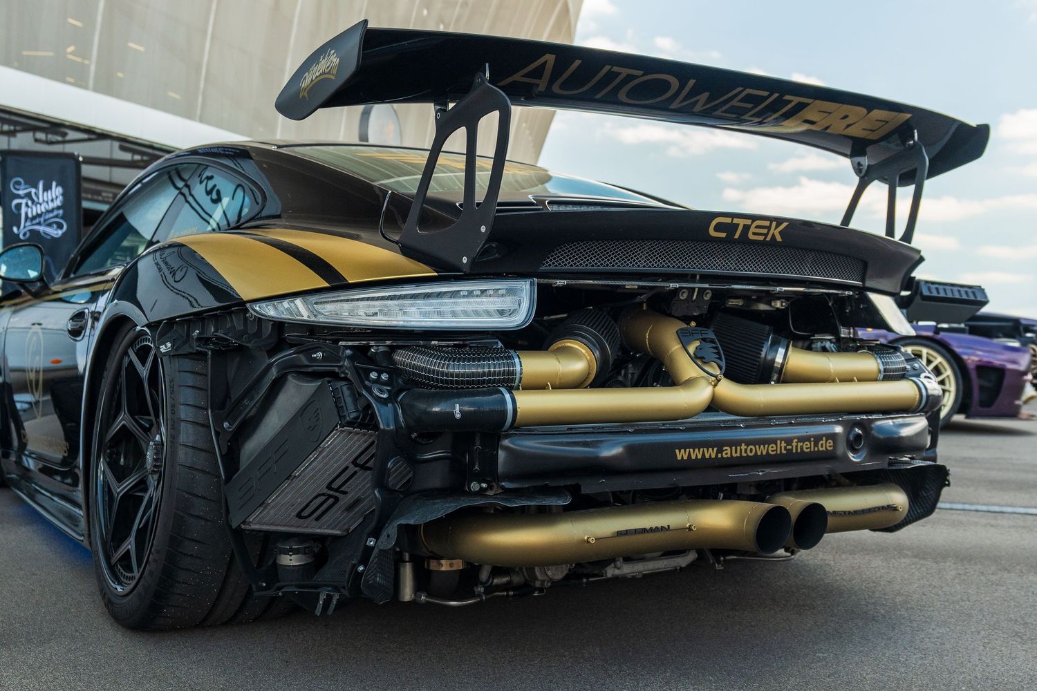 Modified performance car with gold exhaust system and aggressive rear diffuser setup.
