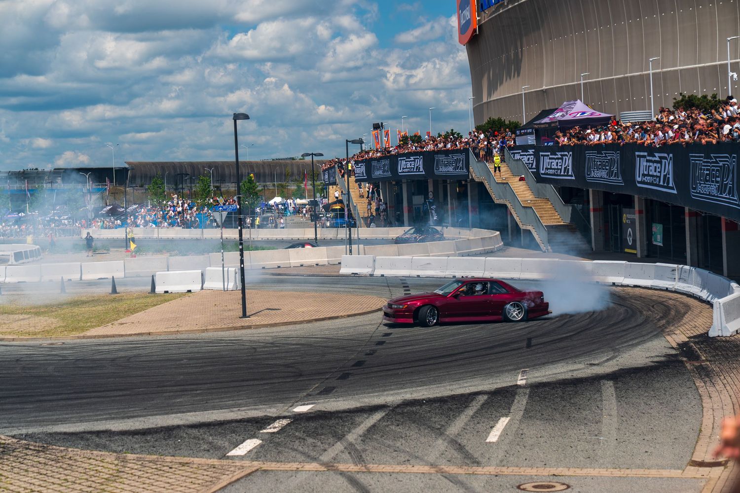 Modified car performing a drift demonstration on a track with clouds in the background.
