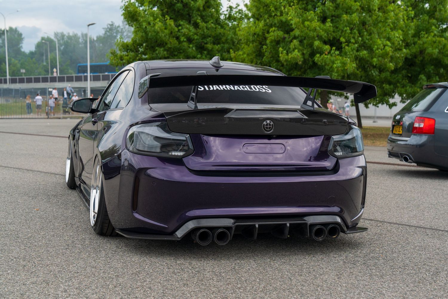 A stanced purple BMW M4 with aggressive body modifications and custom exhaust system.