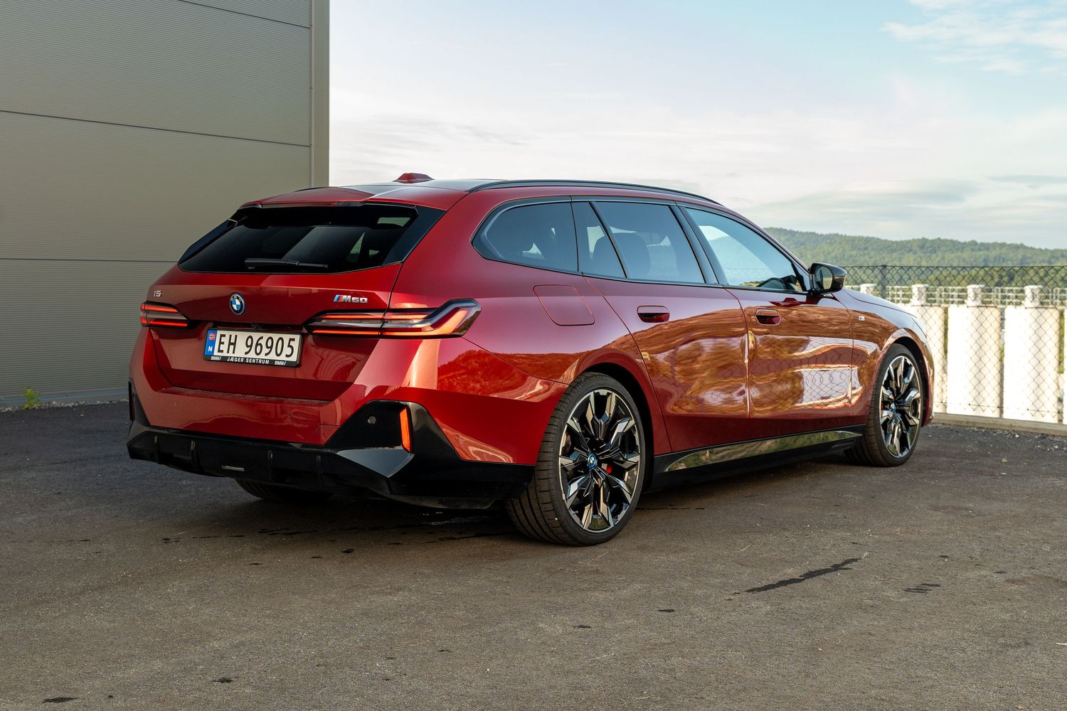A sporty red BMW 3 Series Touring wagon parked against a wall with mountains in the background.