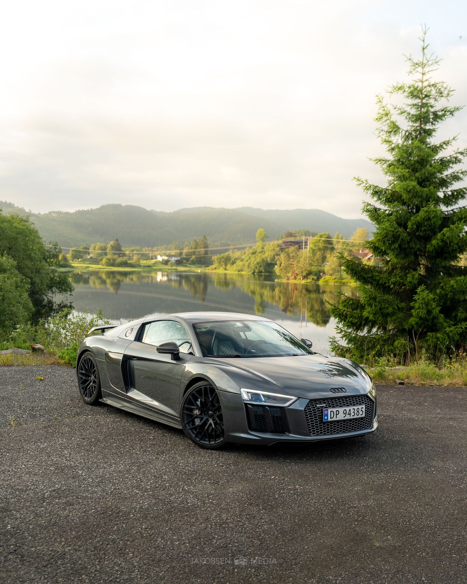 Sleek silver Audi R8 supercar photographed against a scenic mountain landscape with evergreen trees at sunset.