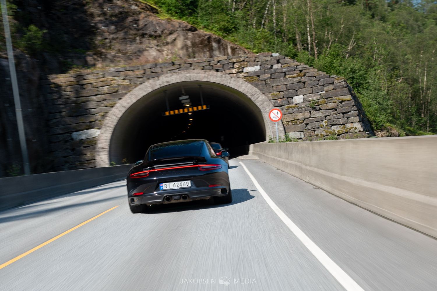 A series of stone tunnels on a mountain road with cars entering and exiting.