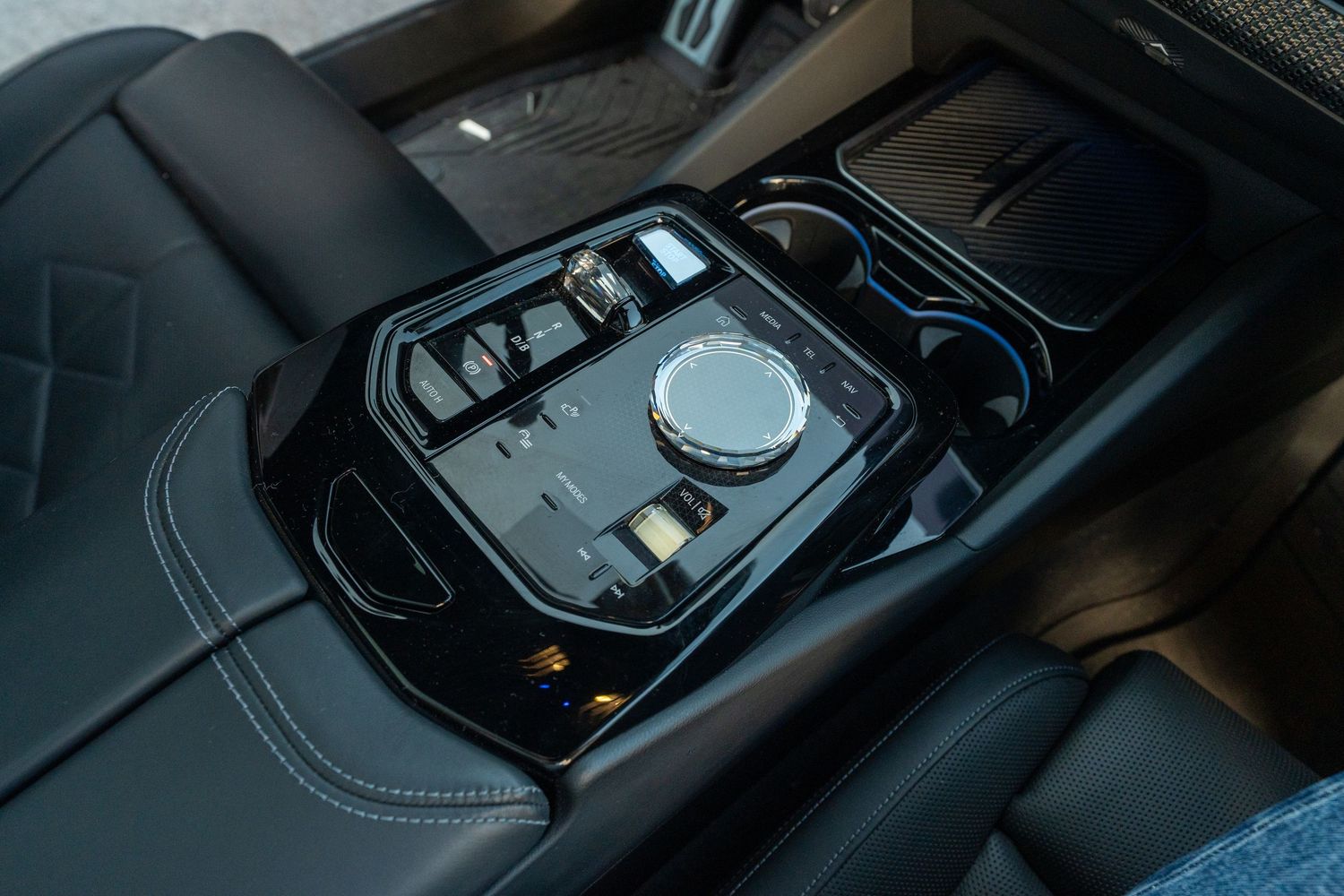 A glossy black interior of a luxury car shows the center console with gear shifter and control knobs.