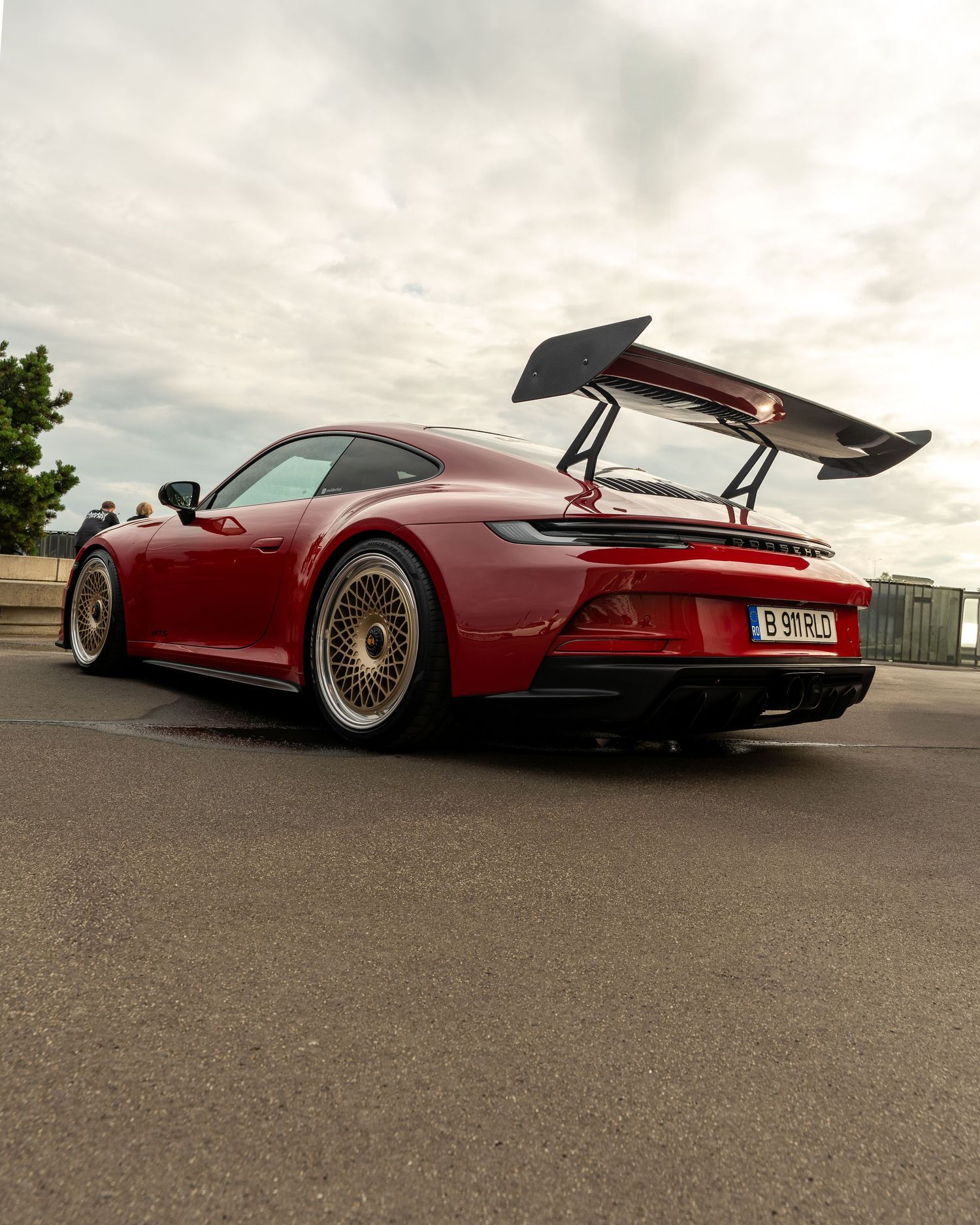 A red Porsche 911 GT3 sports car with a large rear wing parked on a track under cloudy skies.