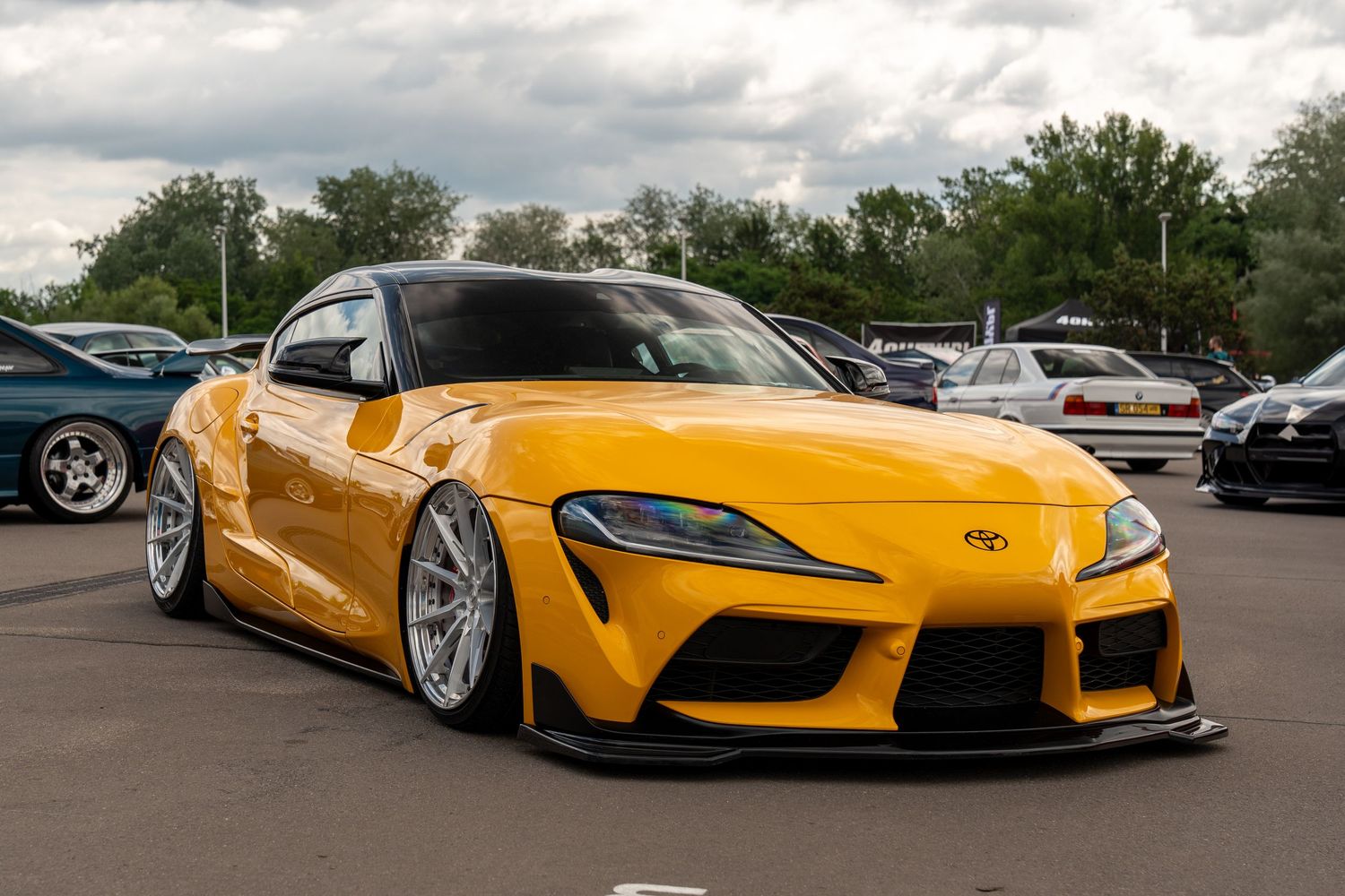 Custom yellow Toyota Supra with wide body kit and stance modifications parked outdoors.