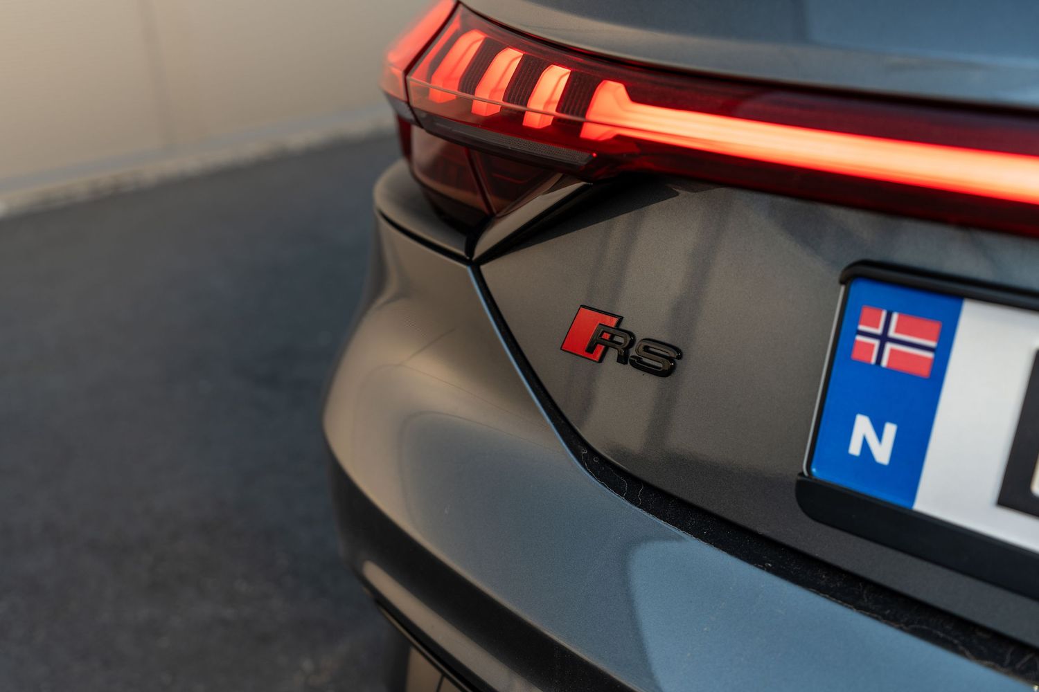 Close-up of an Audi RS model badge and Norwegian license plate on a dark vehicle rear end.