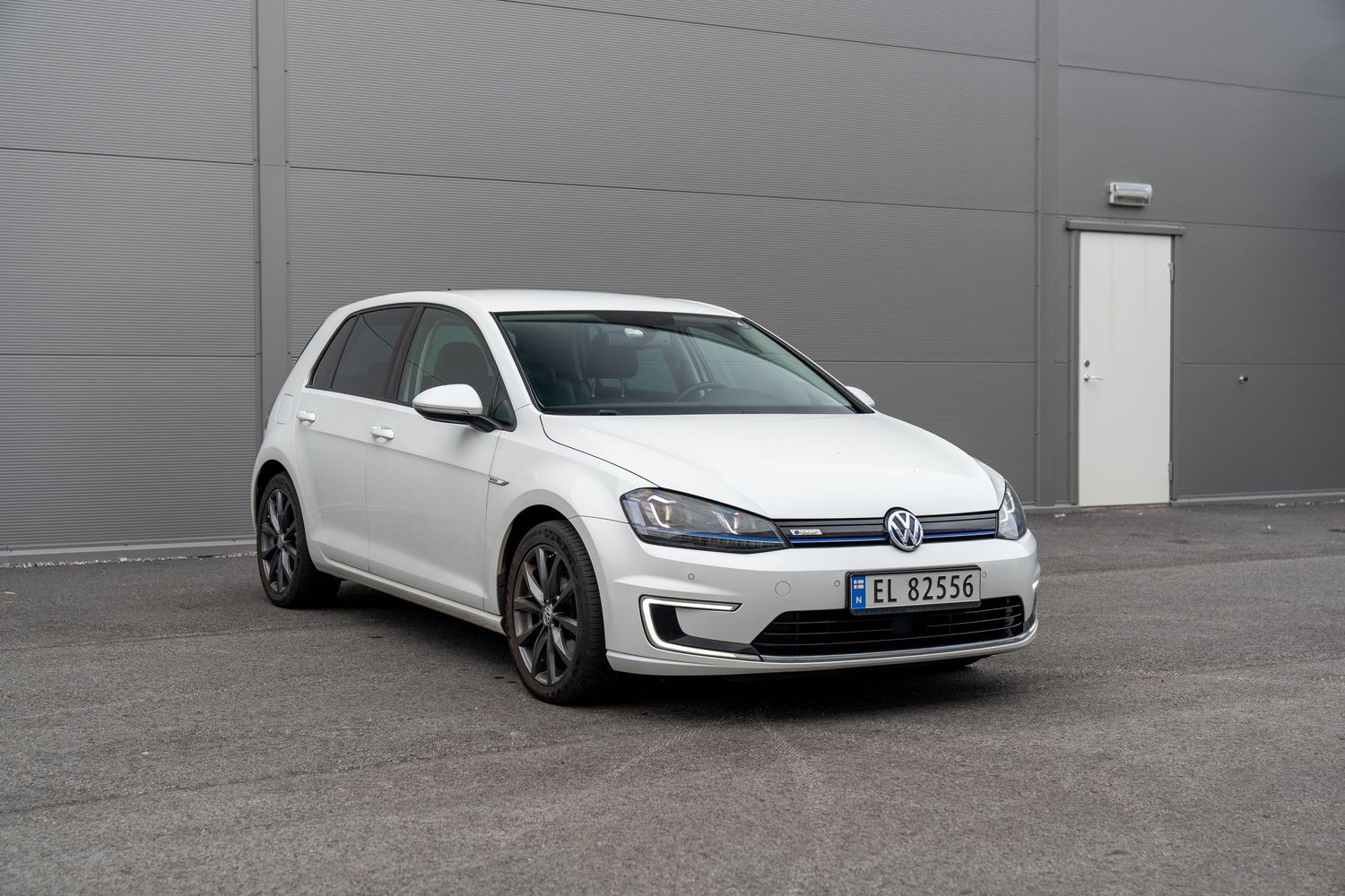A white Volkswagen e-Golf electric hatchback parked in front of a gray wall.
