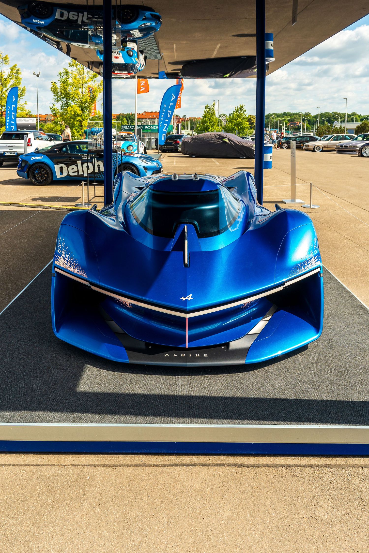 Futuristic blue hypercar concept vehicle with aggressive aerodynamic design displayed under a covered pavilion.