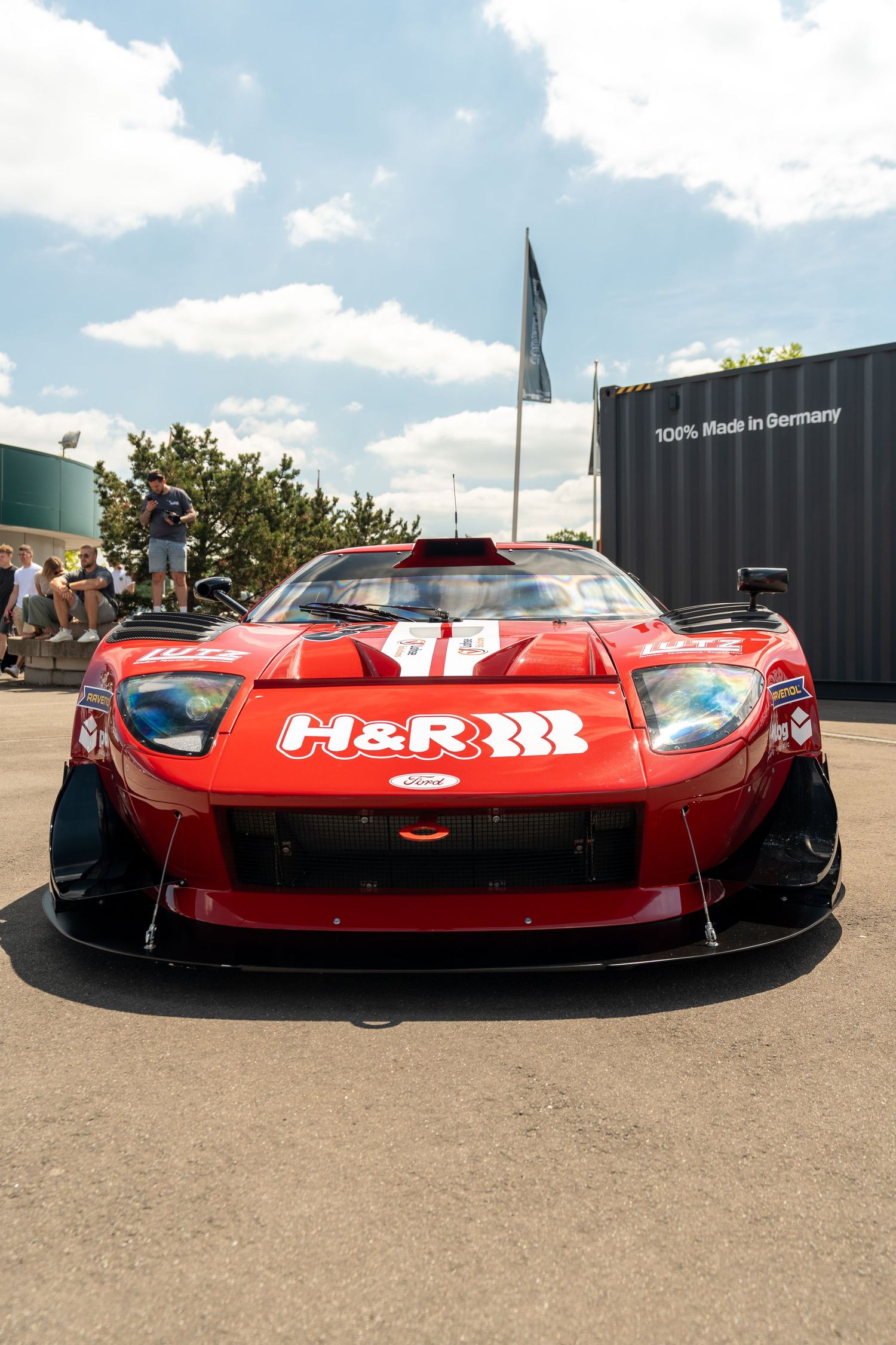 Red Ferrari race car with H&R suspension branding and aggressive aerodynamic modifications on display at an outdoor event.