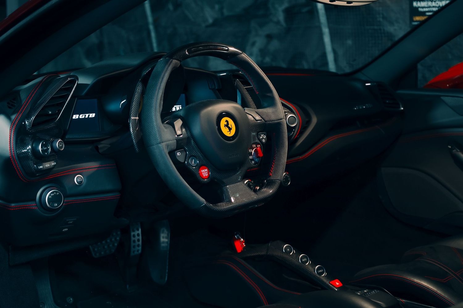 Interior view of Ferrari sports car dashboard and steering wheel with red ambient lighting.