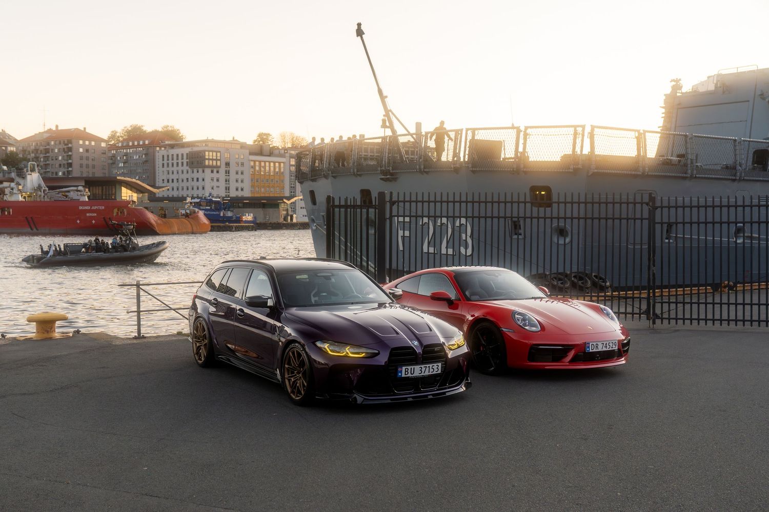 A row of luxury sports cars including Ferrari and Porsche models lined up against a waterfront during sunset.