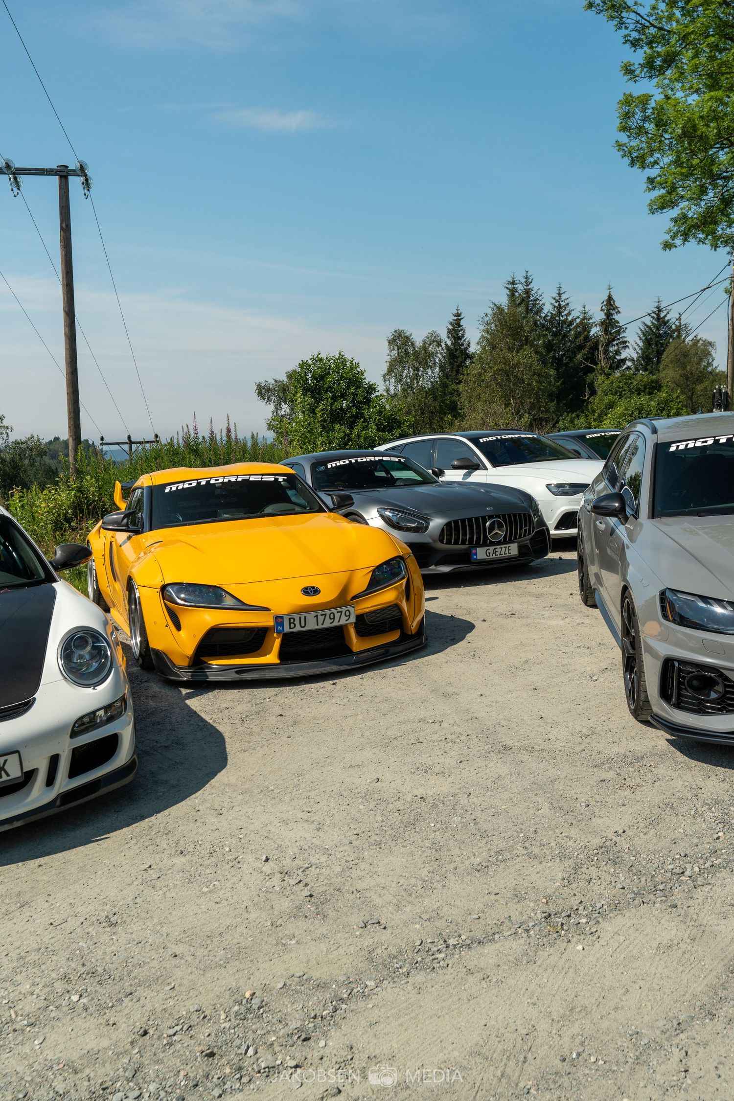 Collection of high-end sports cars including yellow and silver models parked on gravel surface.