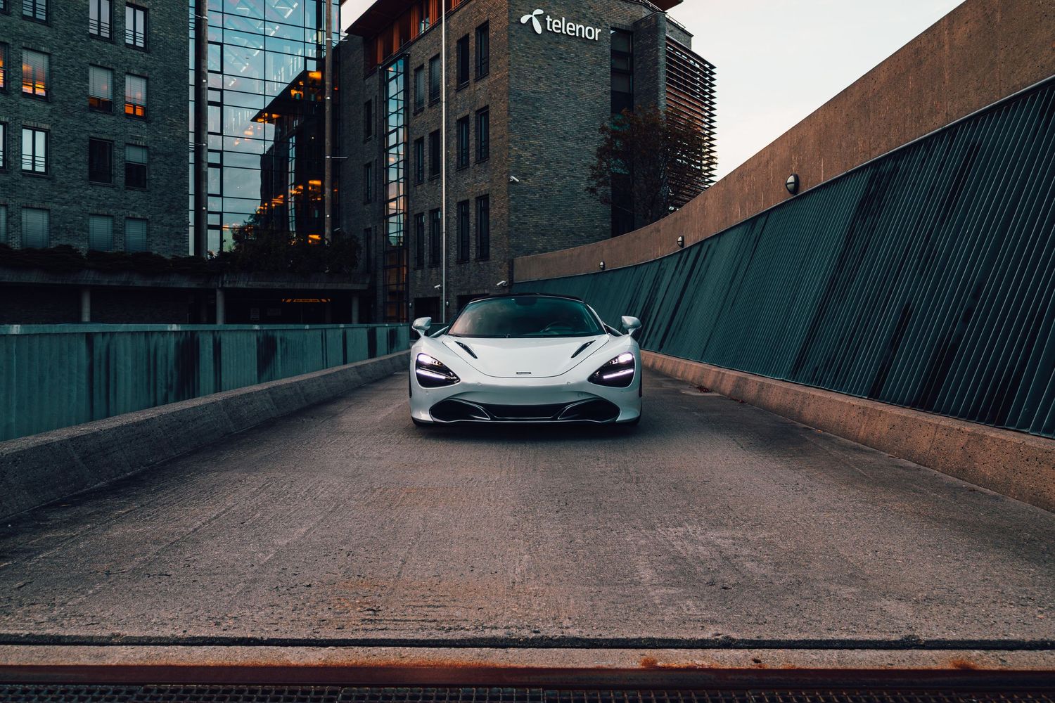 White McLaren sports car positioned in urban setting with industrial architecture.