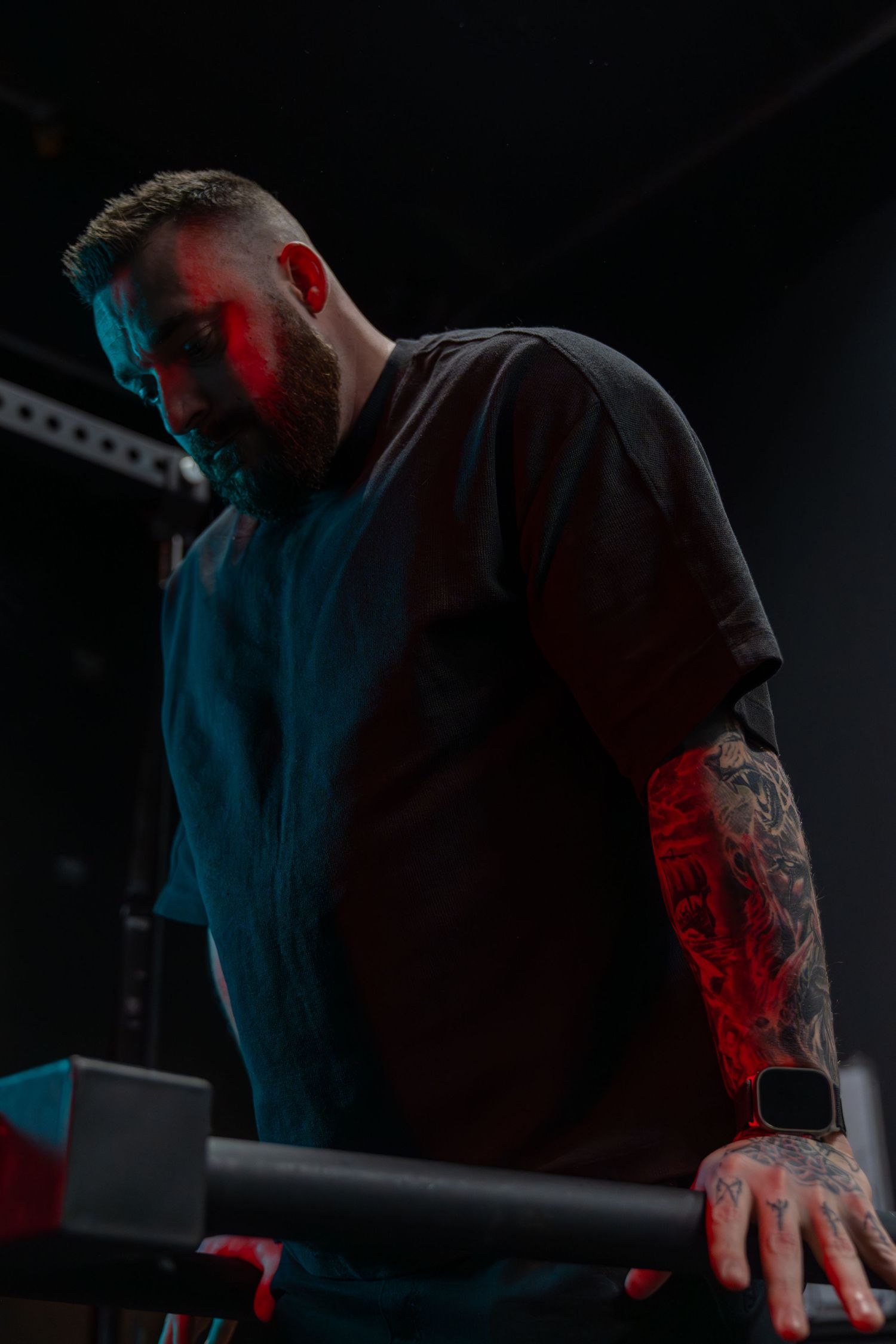 Person with tattoo sleeve leaning over equipment in dark room with colored lighting.