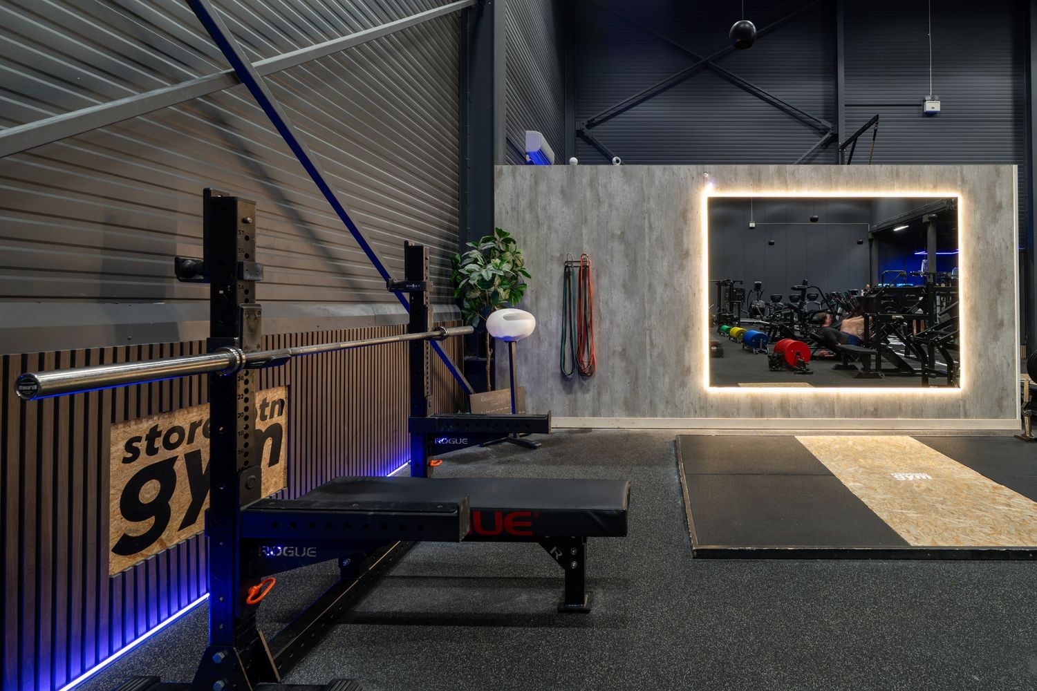 Modern fitness gym interior with weight bench, neon lighting, and concrete wall features in a dark industrial space.