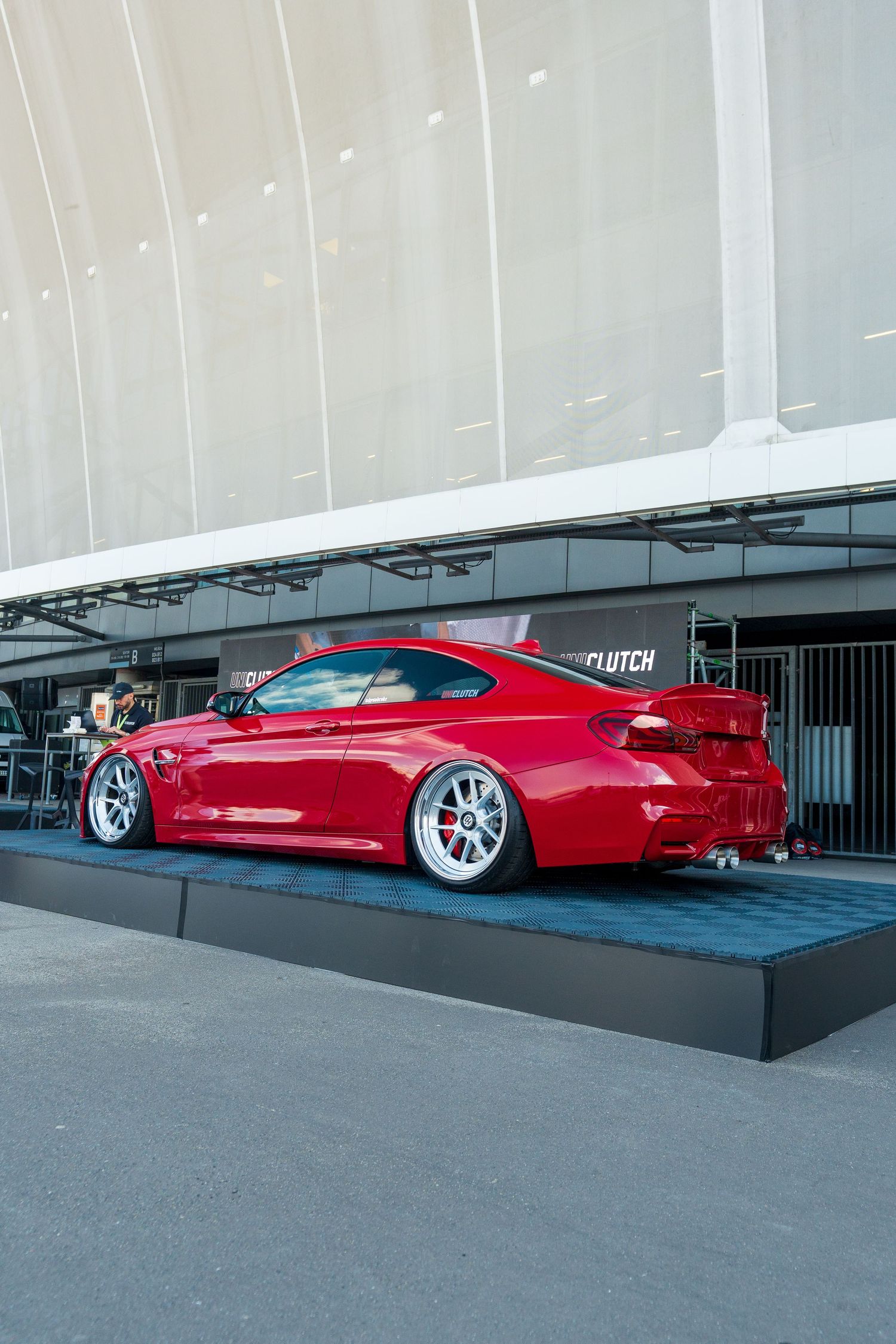 A lowered bright red BMW M6 coupe with custom wheels displayed on a platform at a car show.