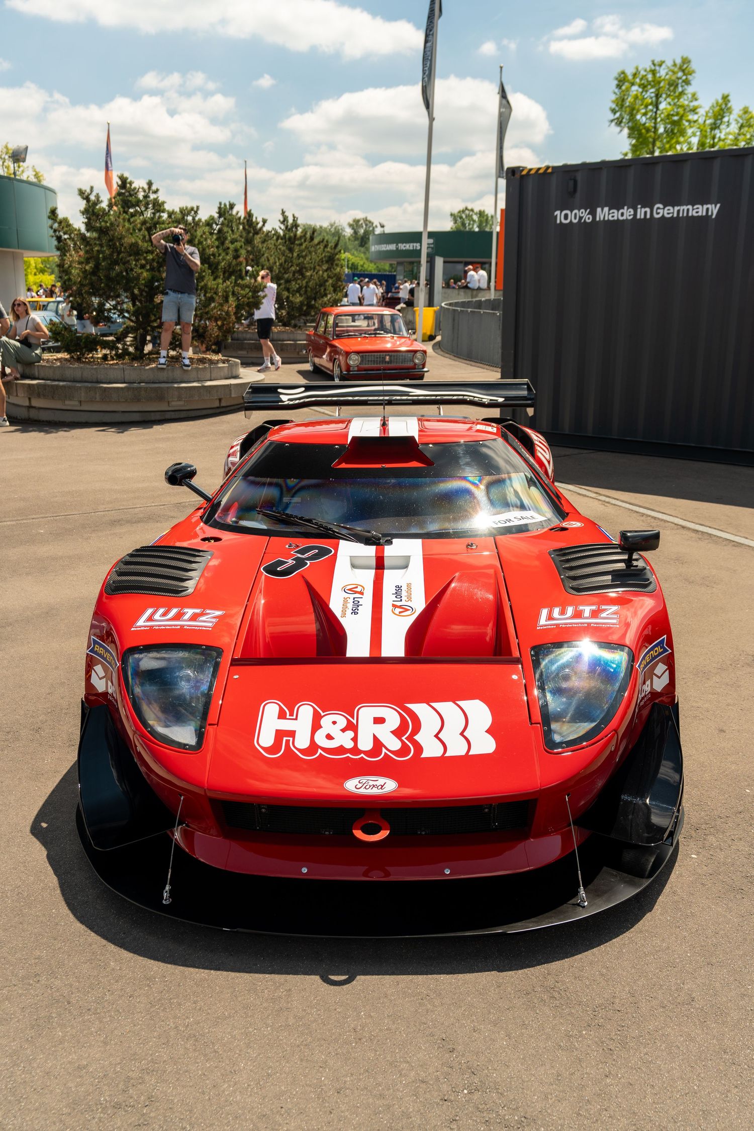 Red Ford GT race car with H&R sponsorship and white racing stripes parked in outdoor display area.