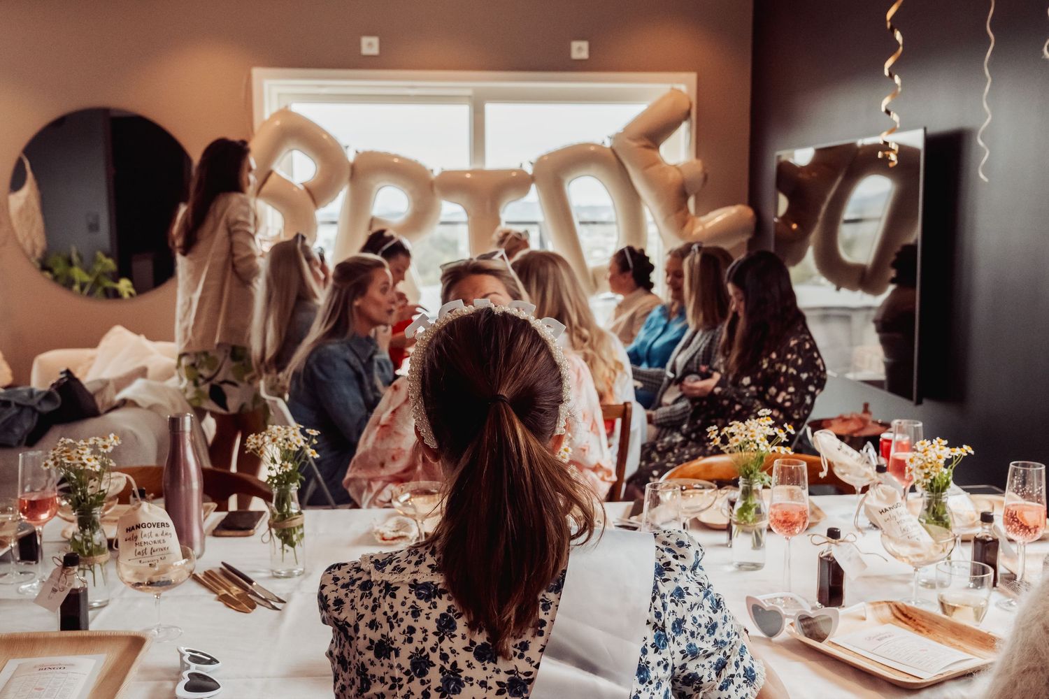 Guests gather around an elegantly decorated table at a celebratory event with flowers and hanging decorations.