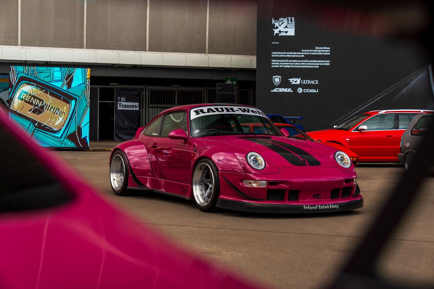 Burgundy modified BMW M3 showcasing aggressive stance and custom wheels in indoor showroom.