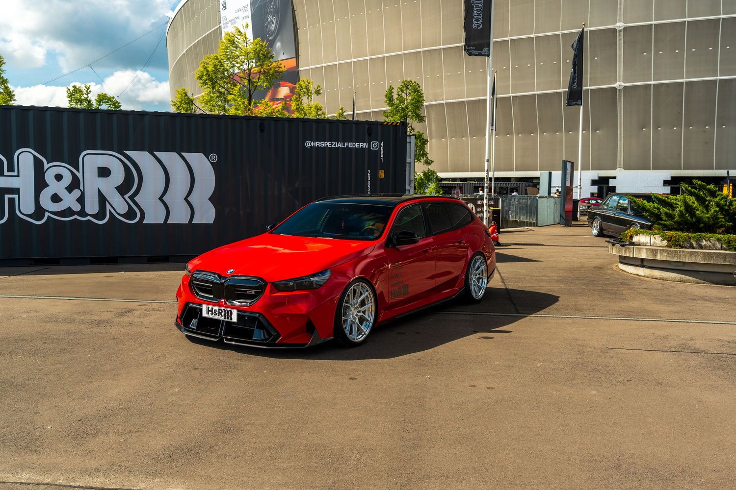 A red Mercedes compact car with custom wheels parked in front of a modern building with graffiti art.