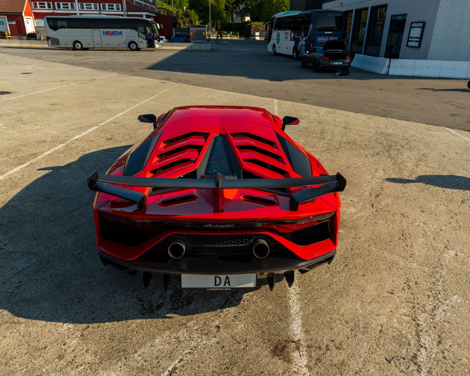Rear view of a red Lamborghini Aventador with aggressive aerodynamic features in a parking lot.