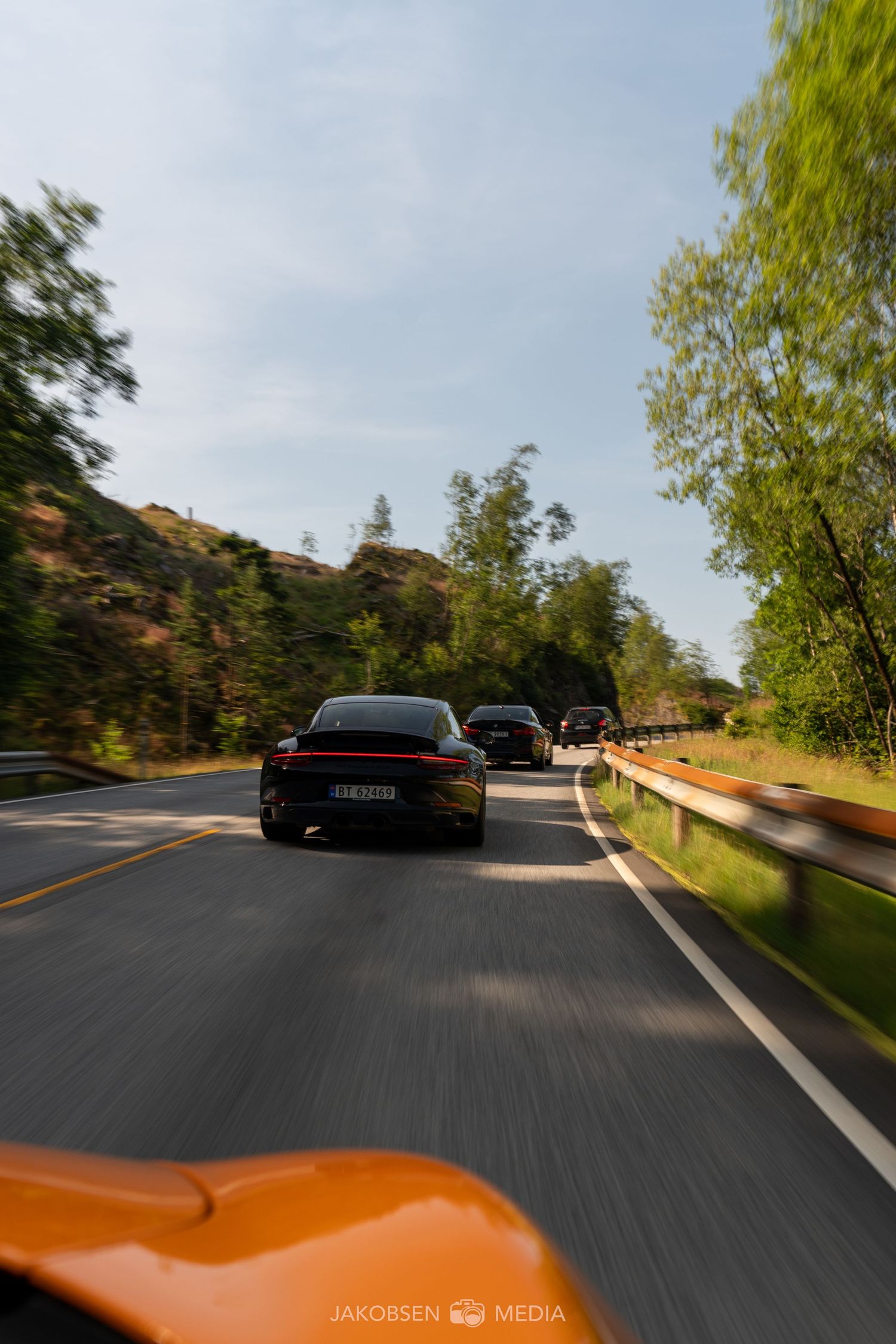 Point-of-view driving shot following luxury sports cars on a winding mountain road.