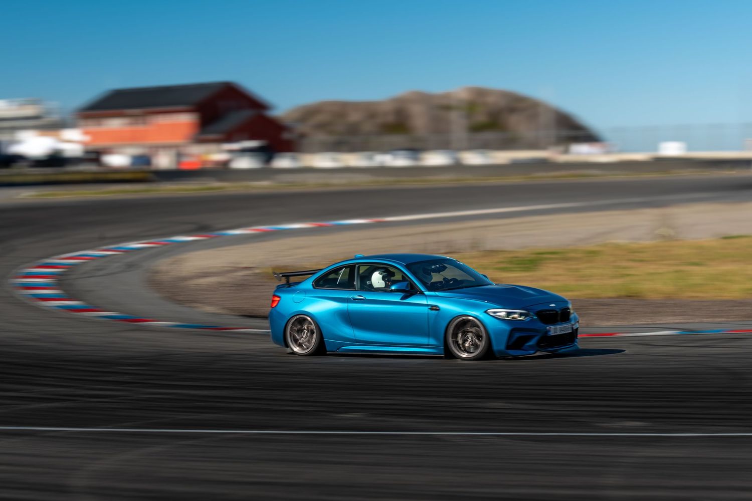 BMW M4 pans across the racetrack in motion with its bright blue exterior color showcasing its sleek design profile.