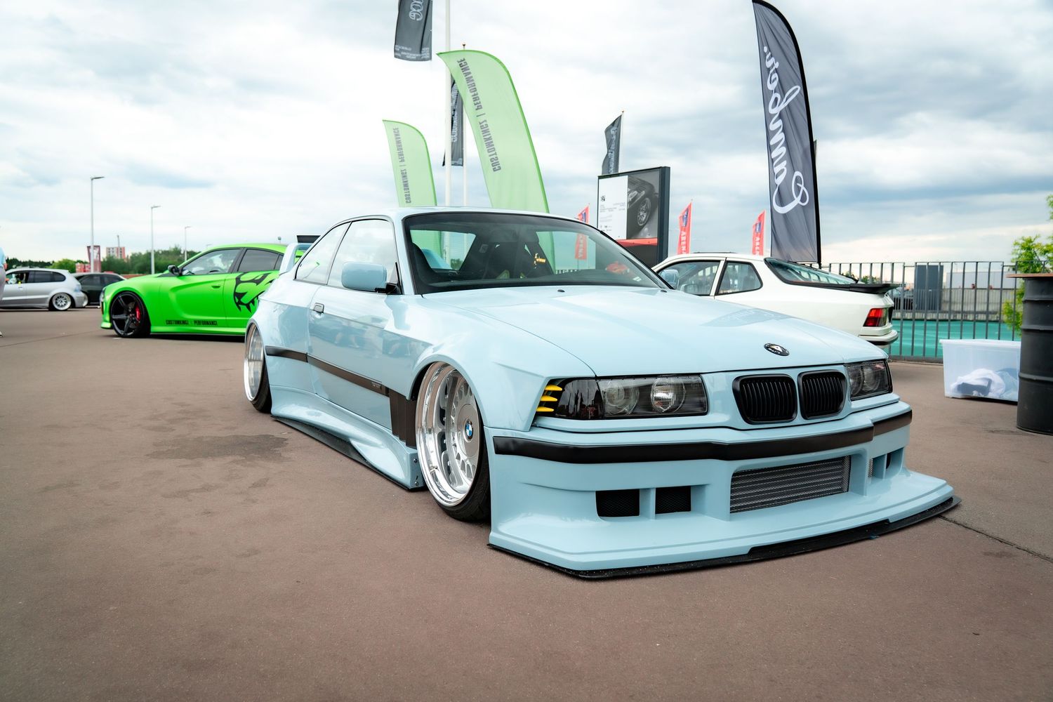 Line of lowered BMW cars in various colors displayed at a car show.