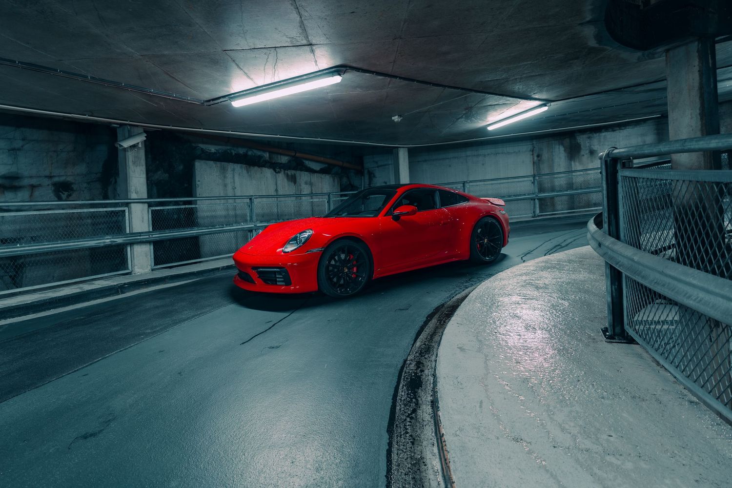 A bright red Porsche GT3 sports car parked in a dimly lit concrete parking garage with moody lighting.