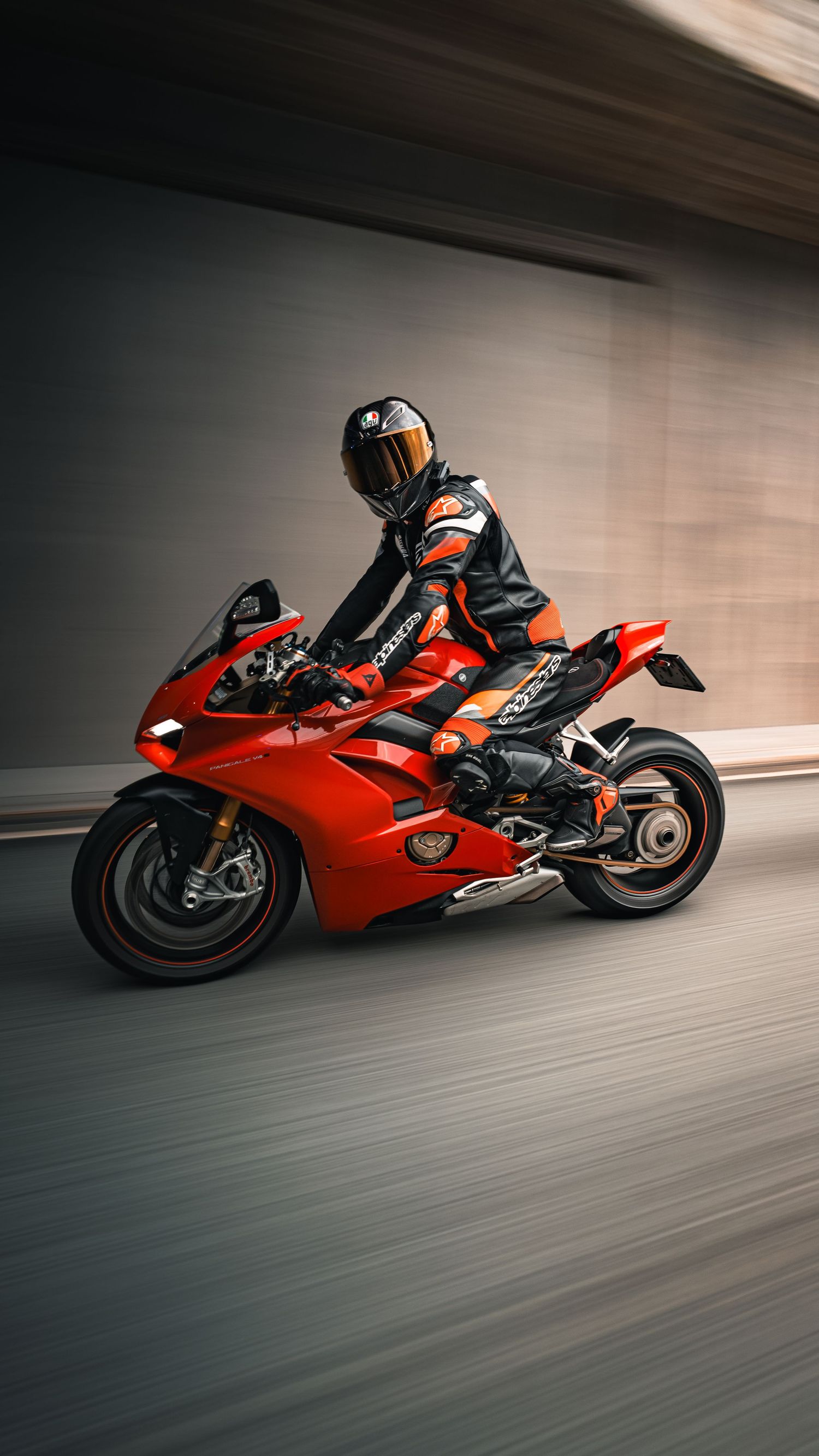 A motorcyclist in black and orange gear rides a red Ducati sportbike at speed through a tunnel with motion blur.