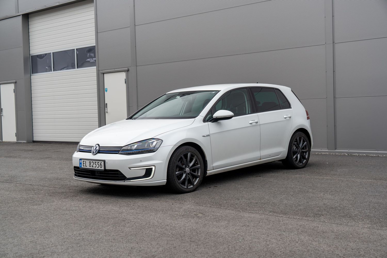 White Volkswagen Golf GTI sport cars parked in front of grey industrial building exterior.