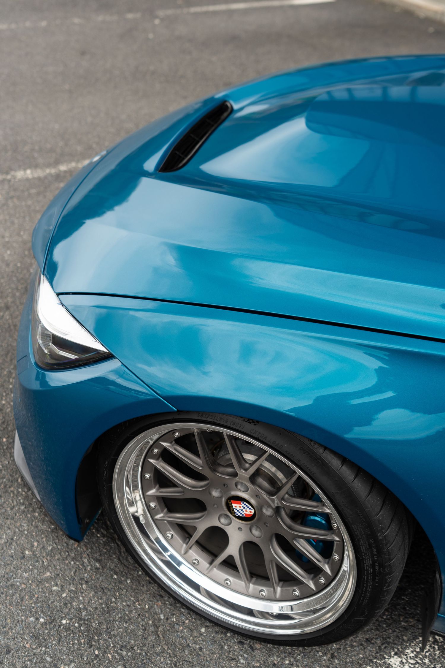 Close-up view of a metallic blue car fender with custom mesh wheels and polished chrome rim details.