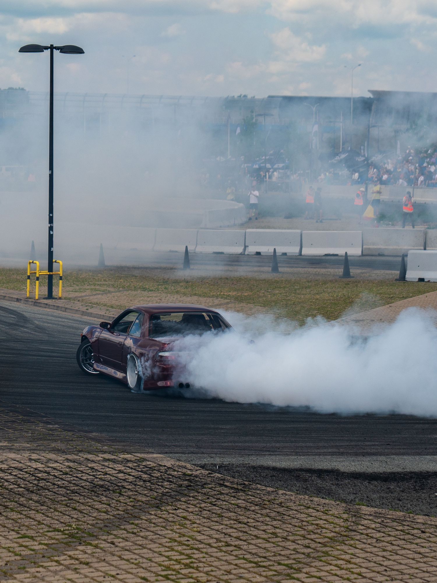 Modified sports car performing drift with smoke on demonstration track.