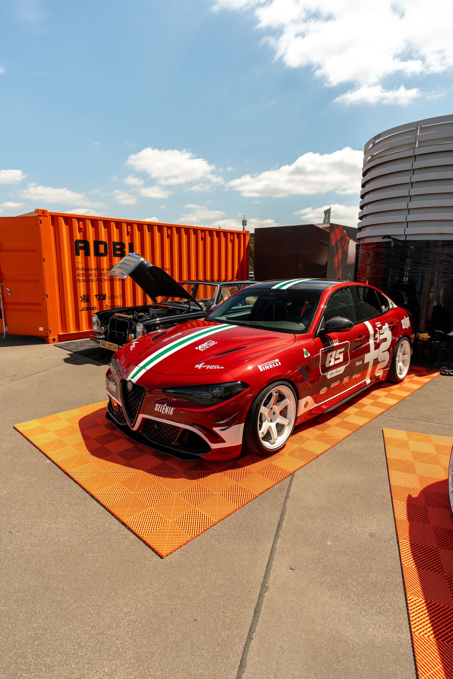 Lowered red sports car displayed on orange platform against industrial backdrop.