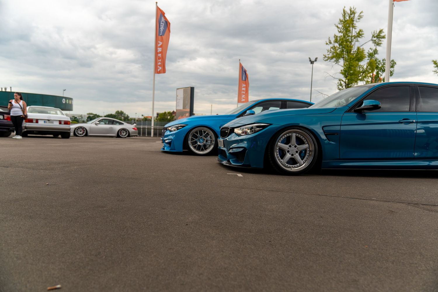 Side profile views of modified BMW vehicles including a bright blue M4 on aftermarket wheels.