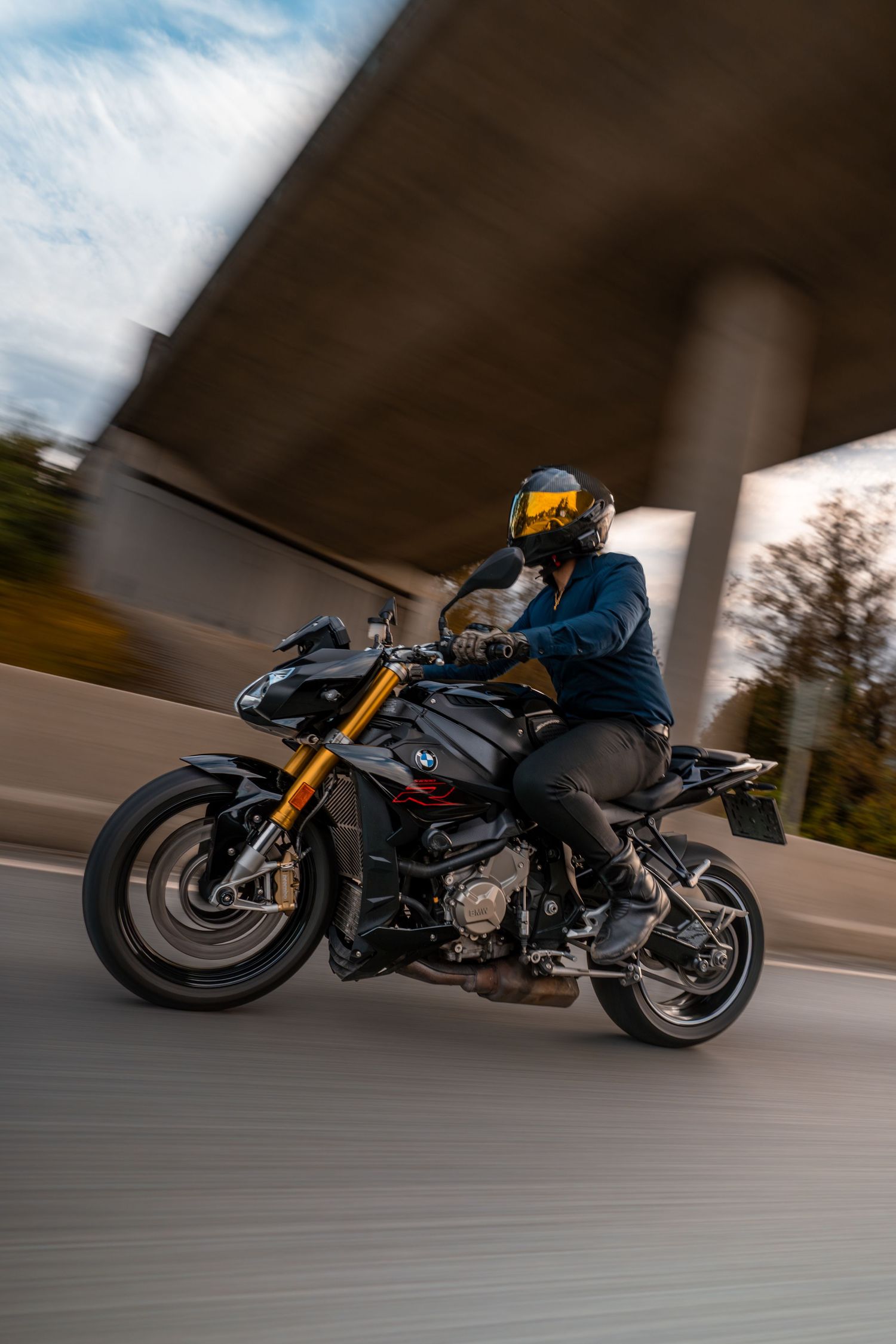 Motorcycle rider speeds down highway on sleek black sports bike with motion blur effect.