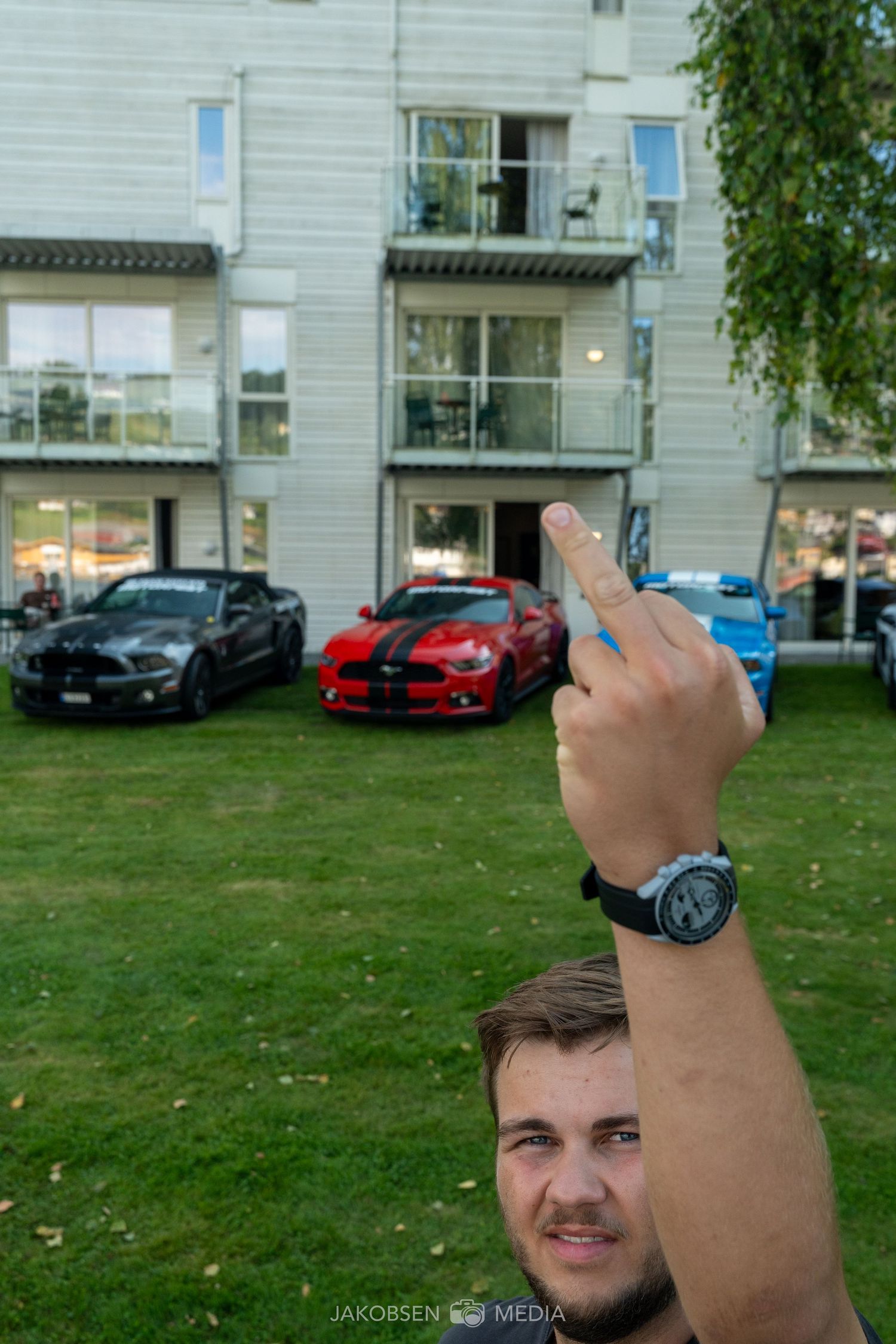 Luxury cars parked on grass in front of modern apartment buildings.