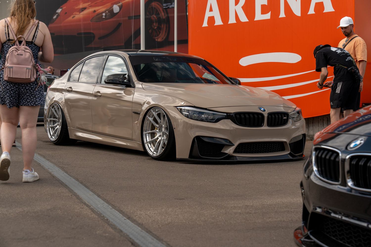 Lowered BMW M3 in champagne color with custom wheels parked at car show.