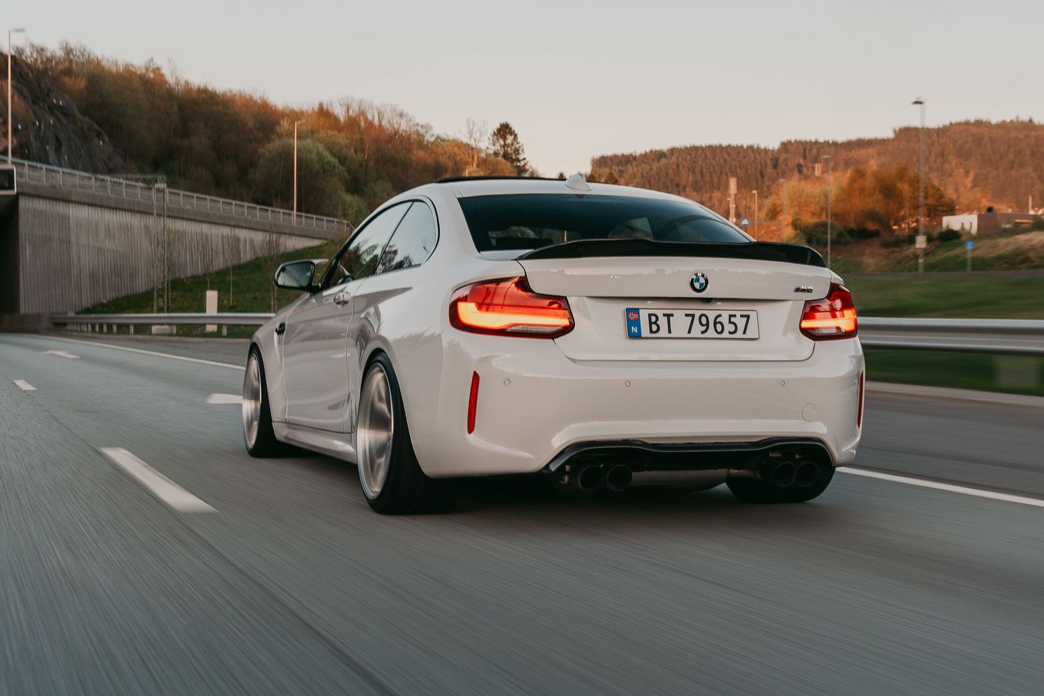 White BMW M2 rear view showing distinctive taillights while driving on mountain road.