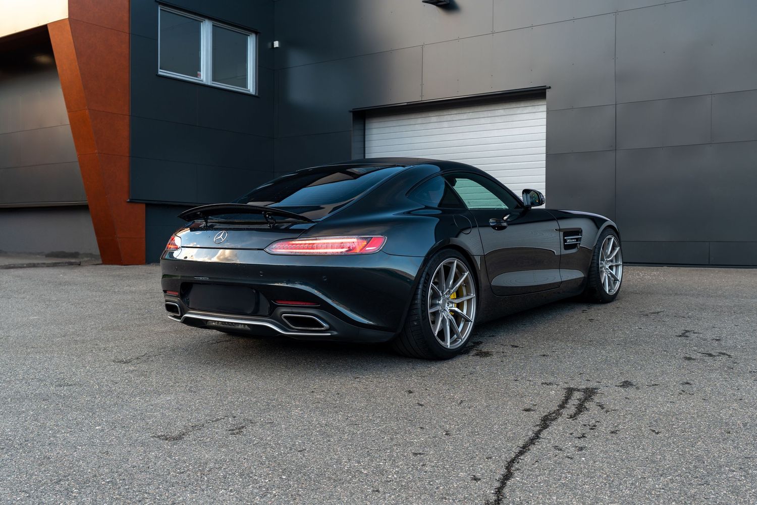 Black Mercedes-AMG GT sports car parked in front of industrial garage doors with modern architecture.