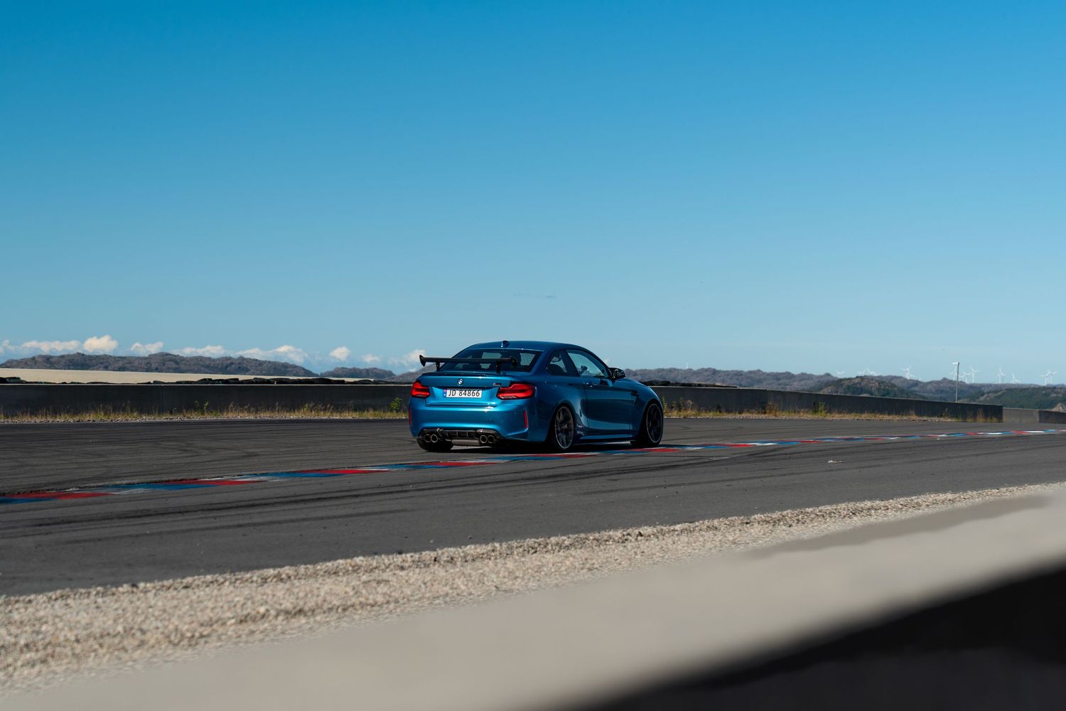 Blue Porsche sportscar parked on a desert road with mountains in background under clear sky.