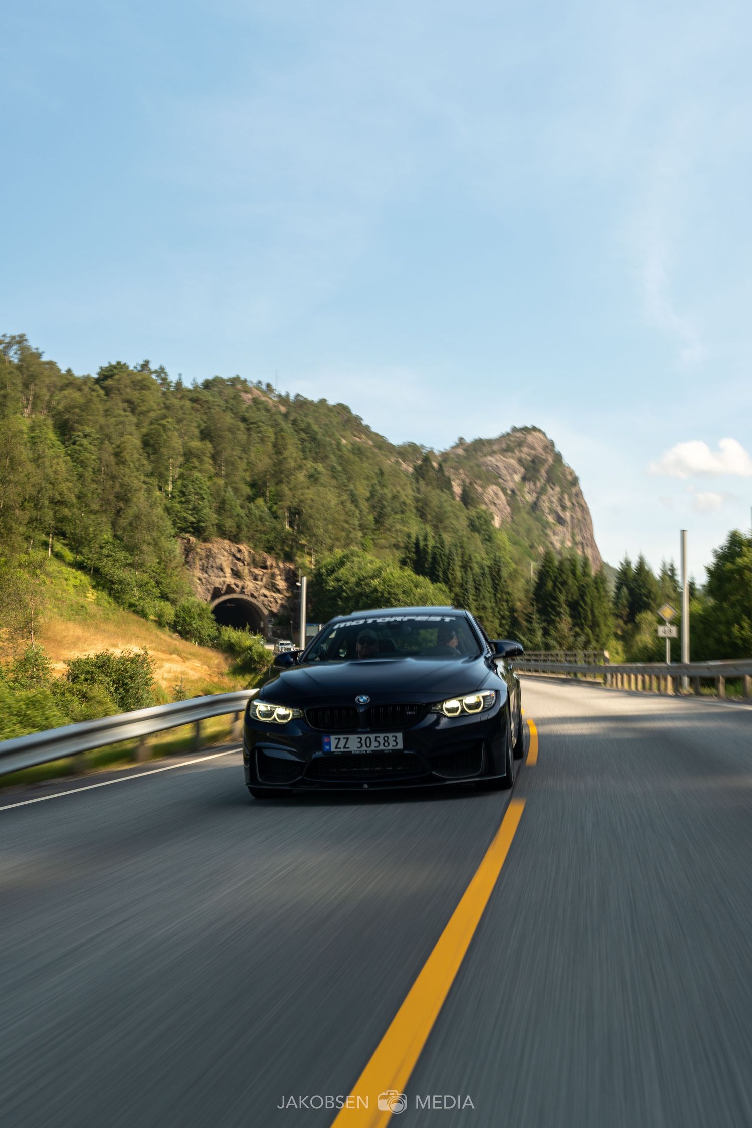 Black sports car driving on a scenic mountain road with rocky cliffs and blue skies.