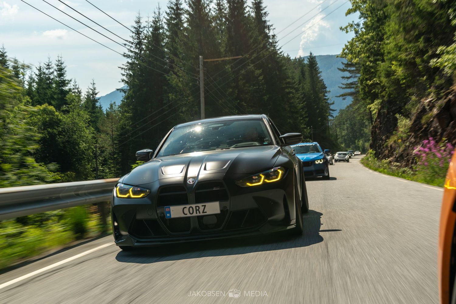Sports cars driving on mountain road surrounded by evergreen forest.