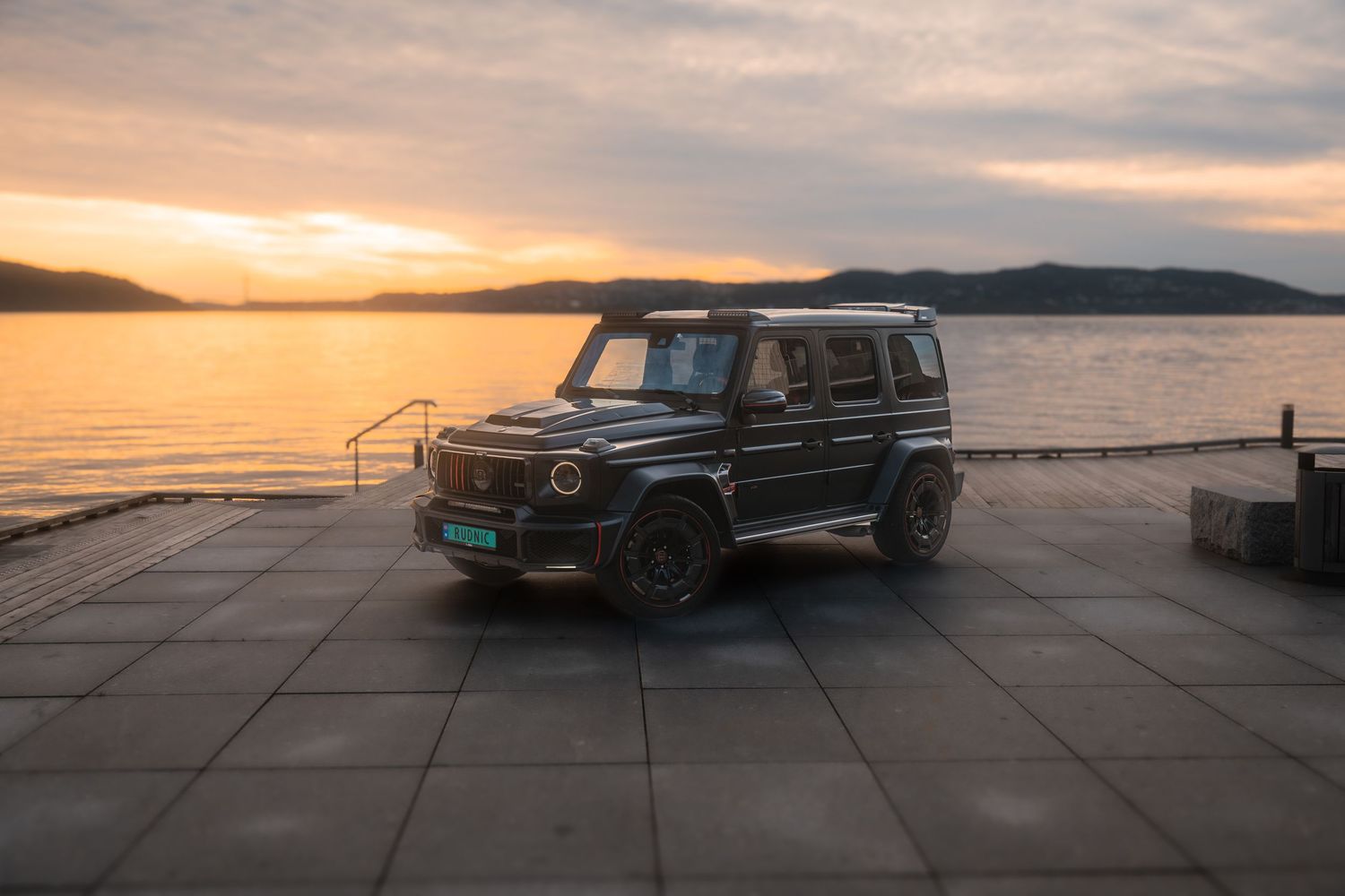 Mercedes G-Wagon silhouetted against dramatic coastal sunset with mountains in the background.