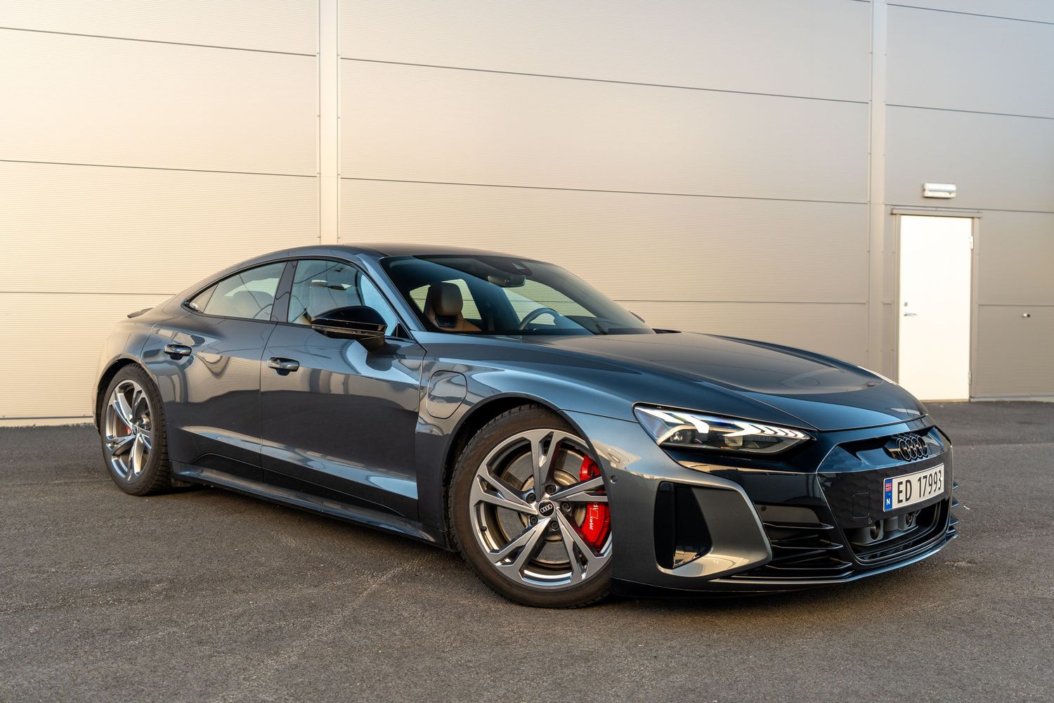 Side profile of a metallic grey Audi RS e-tron GT with red brake calipers against white wall.