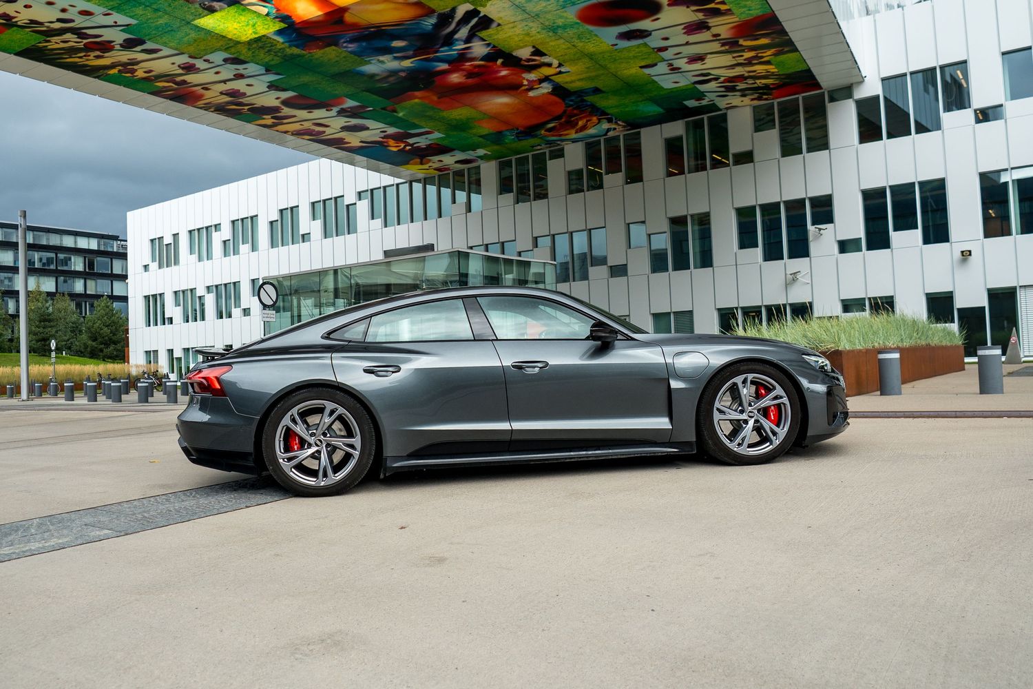 Gray luxury sports sedan parked beside a modern building with colorful ceiling art.