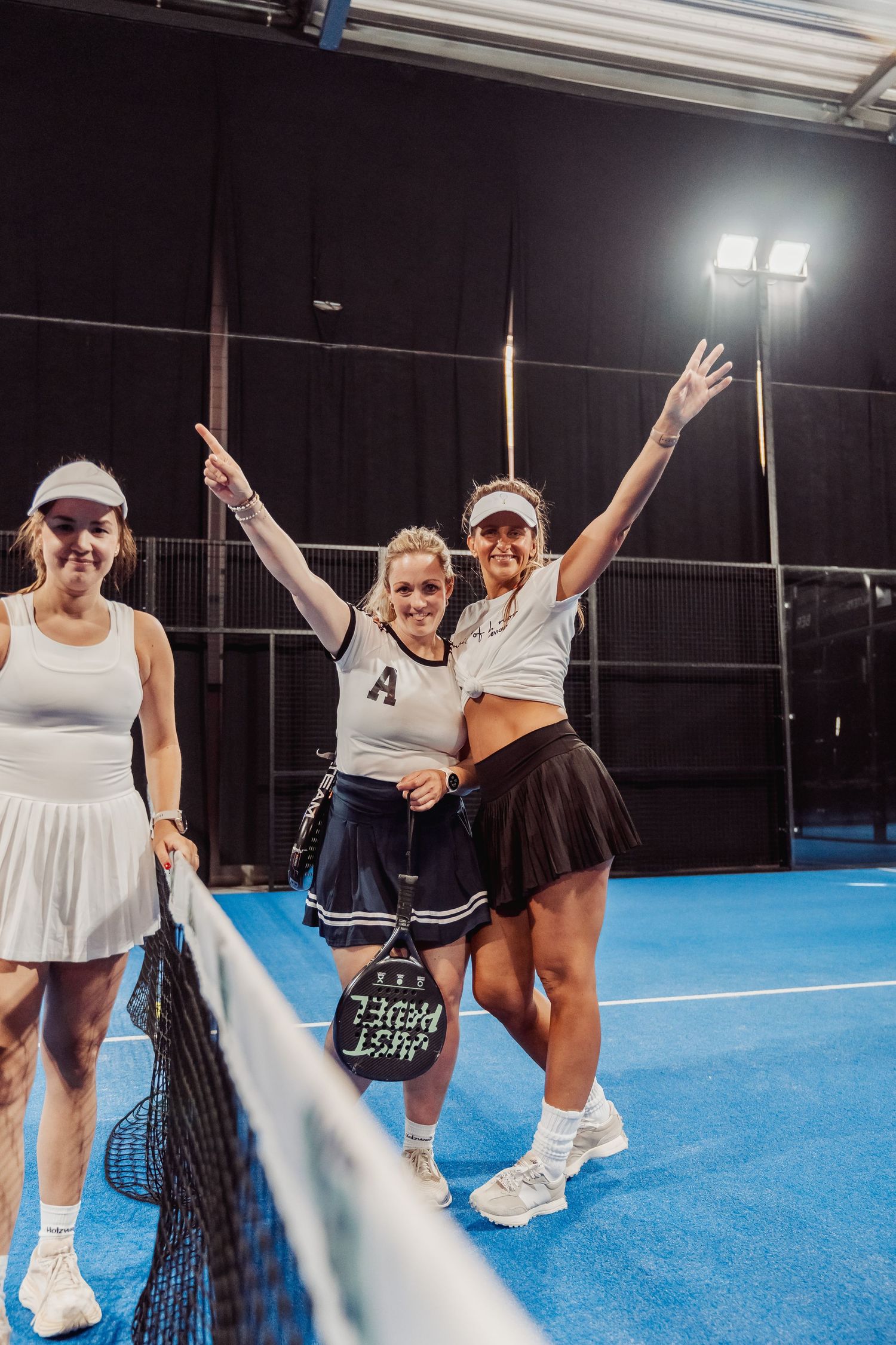 Three players posing with tennis rackets on blue indoor court.