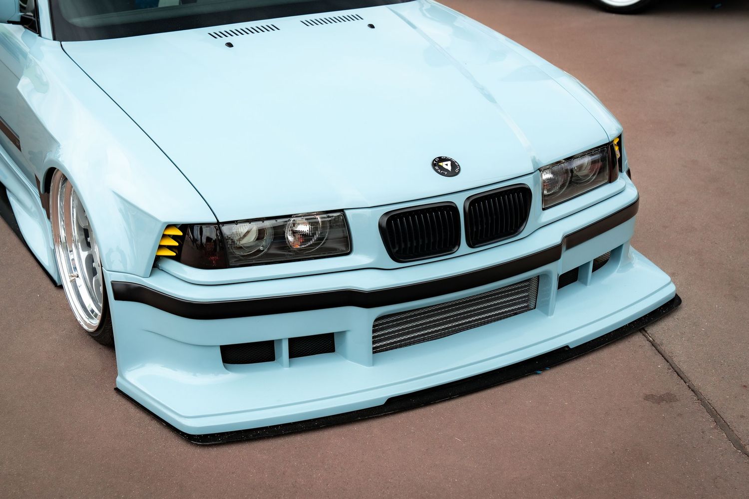 Light blue BMW E36 with modified front bumper and custom body kit.